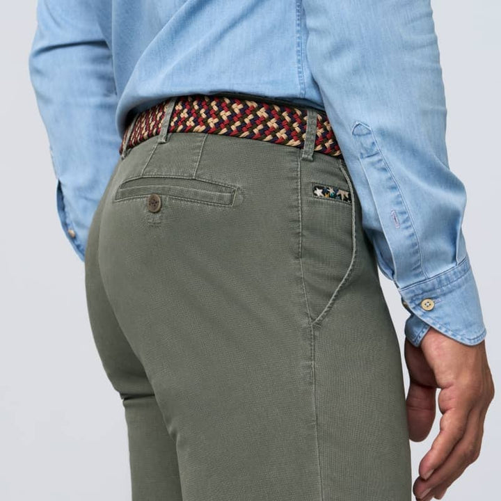 Person wearing green pants and a light blue shirt with a patterned belt on a white background